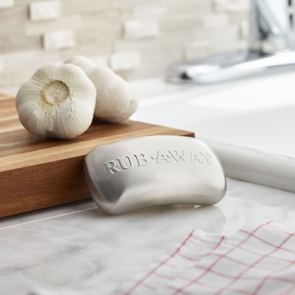 The stainless steel soap bar resting against a cutting board with two heads of garlic on it