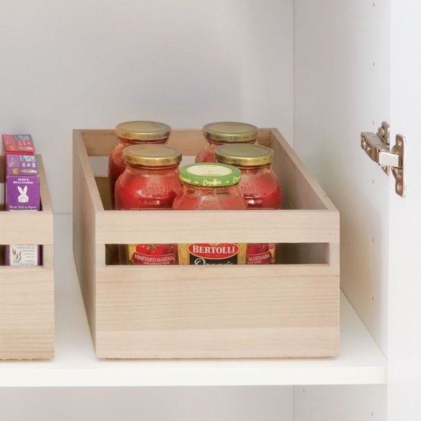 the wooden bin in a cabinet filled with tomato sauce jars