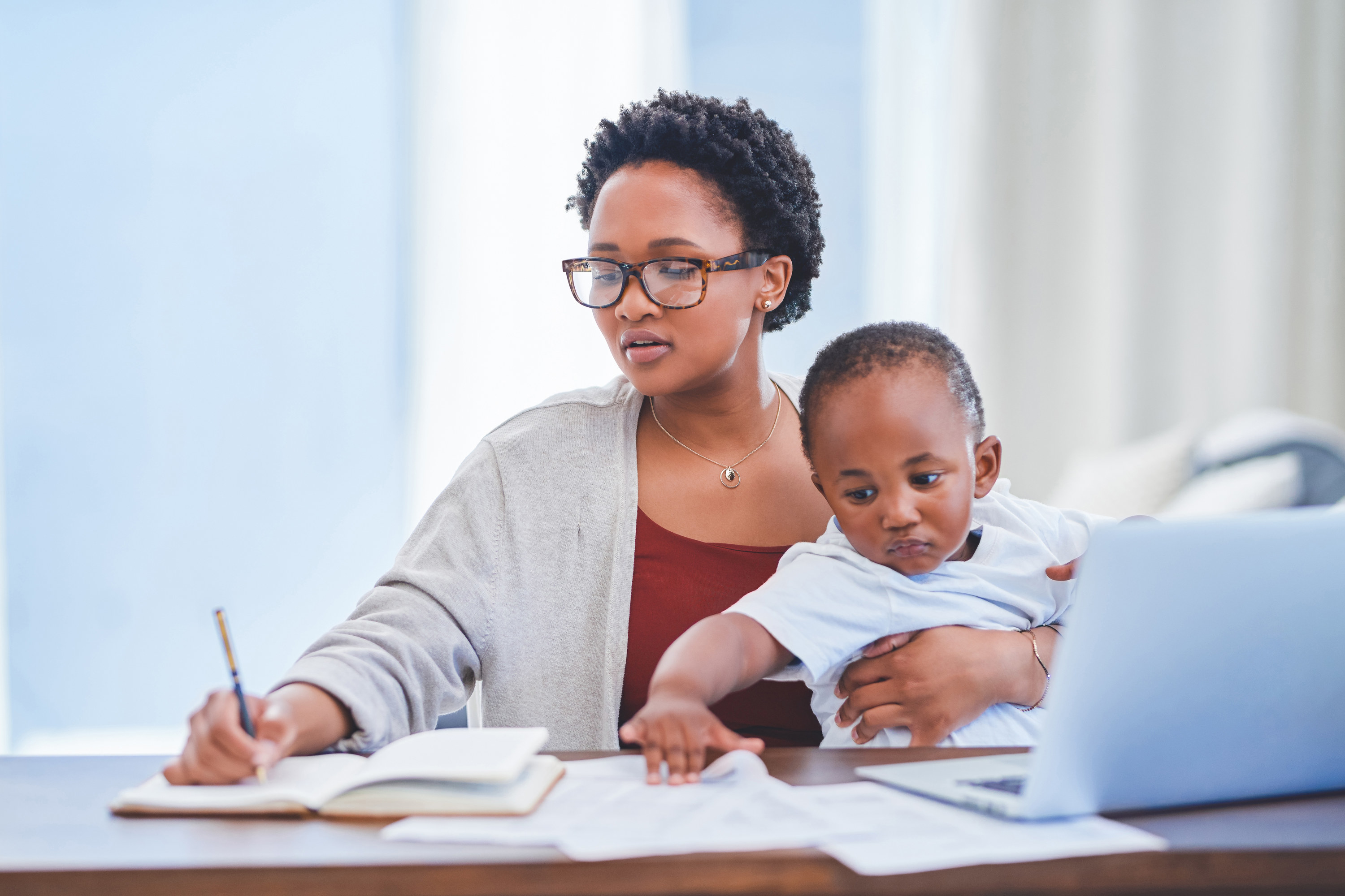 Working mom holding a baby while writing at her desk