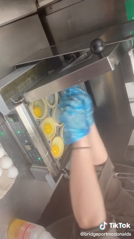 a person cracking eggs in round rings over a griddle