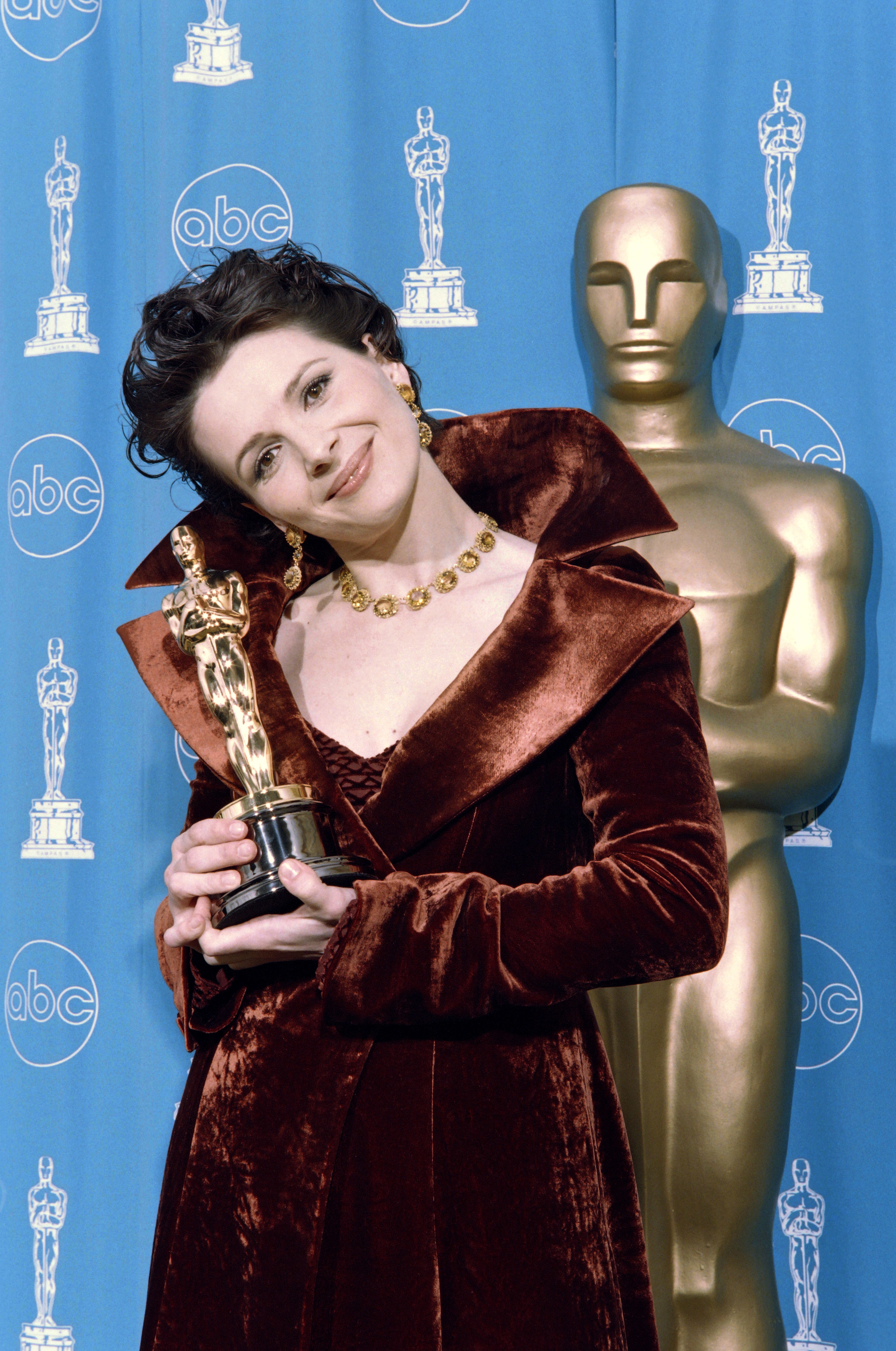 Juliette Binoche smiles as she holds her Best Supporting Actress Oscar in 1997