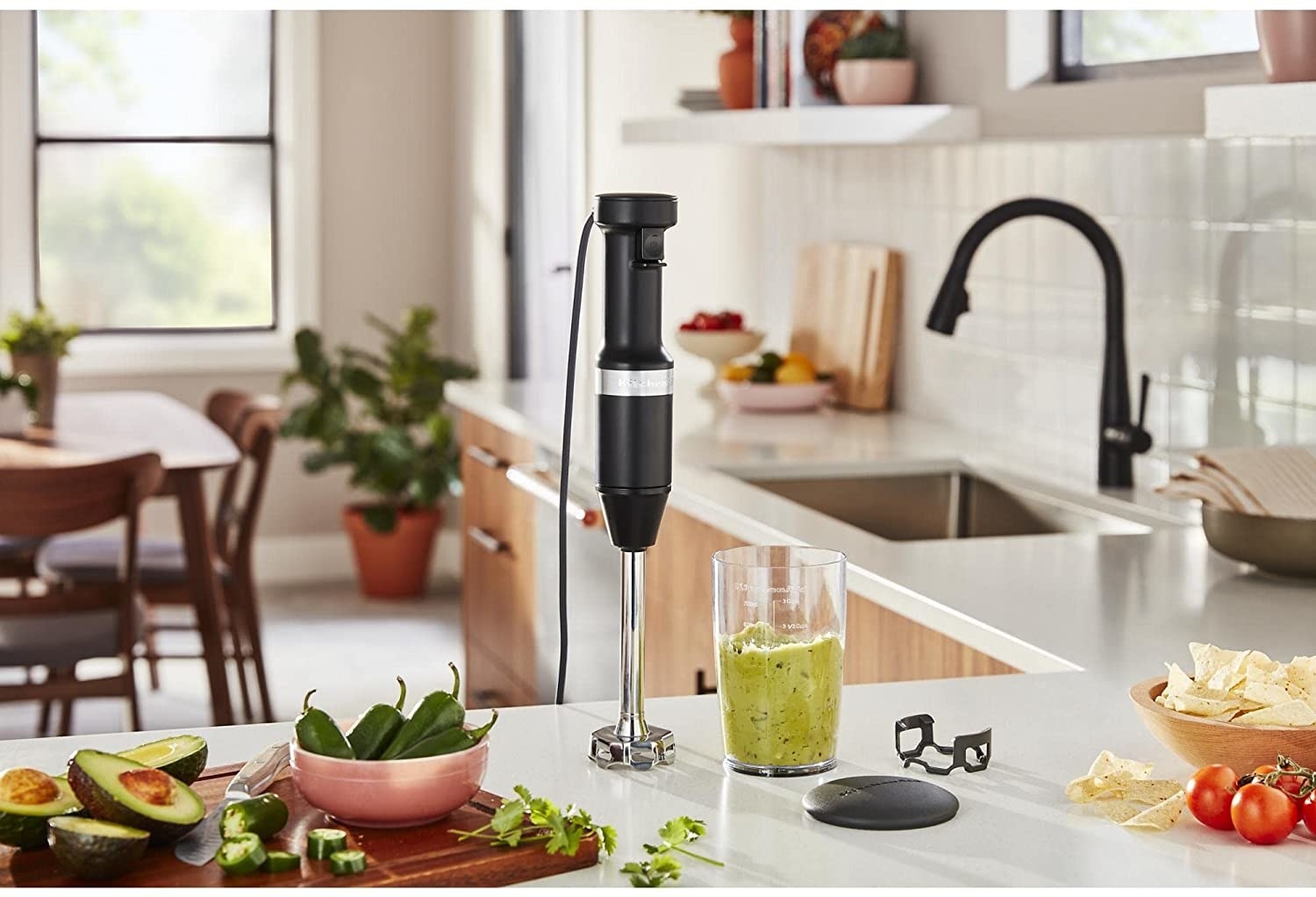The hand blender on a kitchen counter surrounded by guacamole ingredients