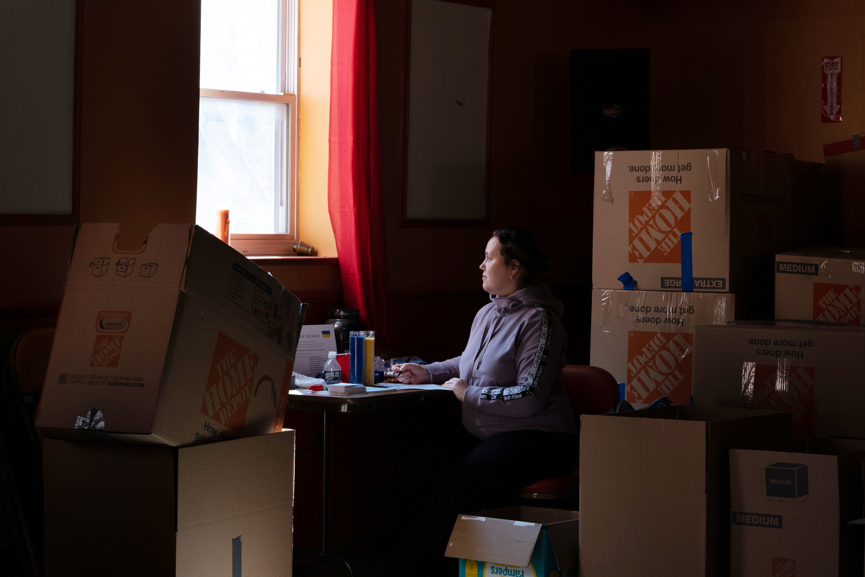 A woman sits at a desk surrounded by cardboard boxes 