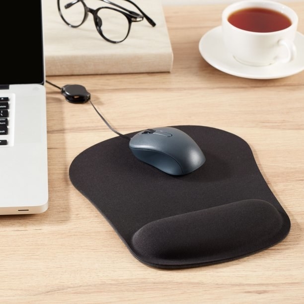 Black cushioned mouse pad on wooden table with mouse on it next to laptop