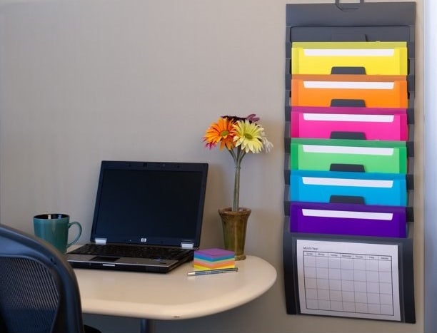 Wall organizer with multi colored folders on wall next to desk with laptop on it