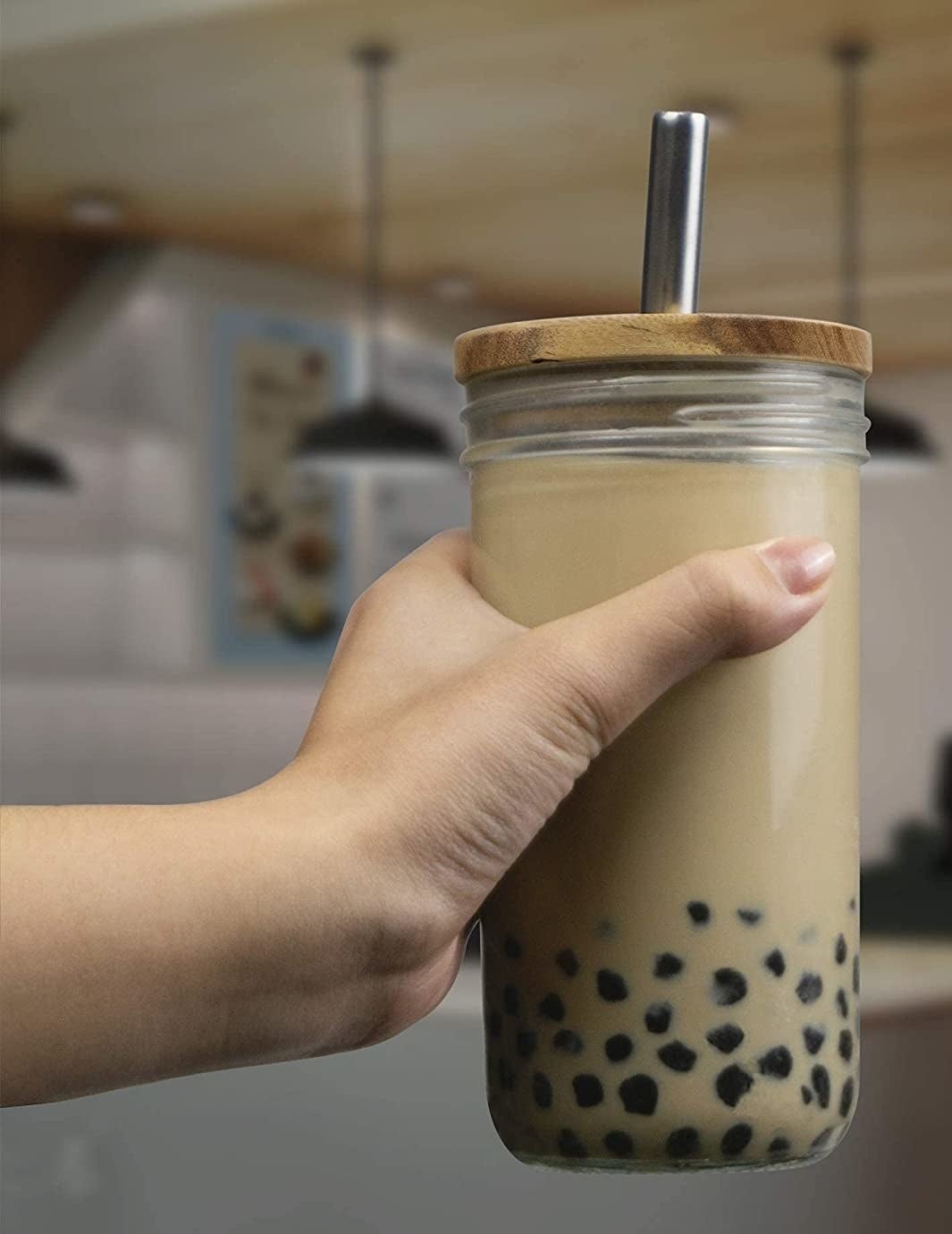 A person holding up the glass tumbler with bubble tea in it