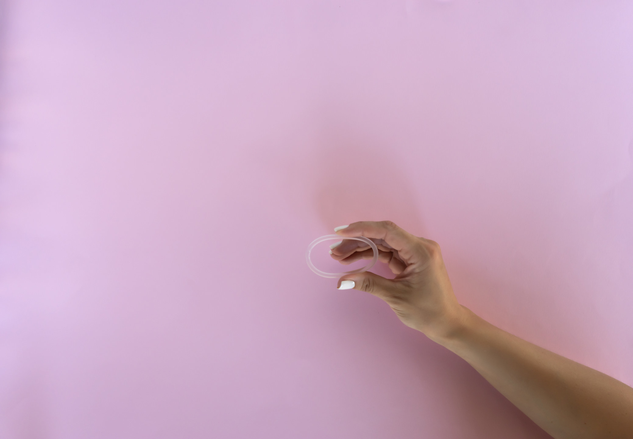 A stock image of someone holding up a birth control ring in front of a pink background