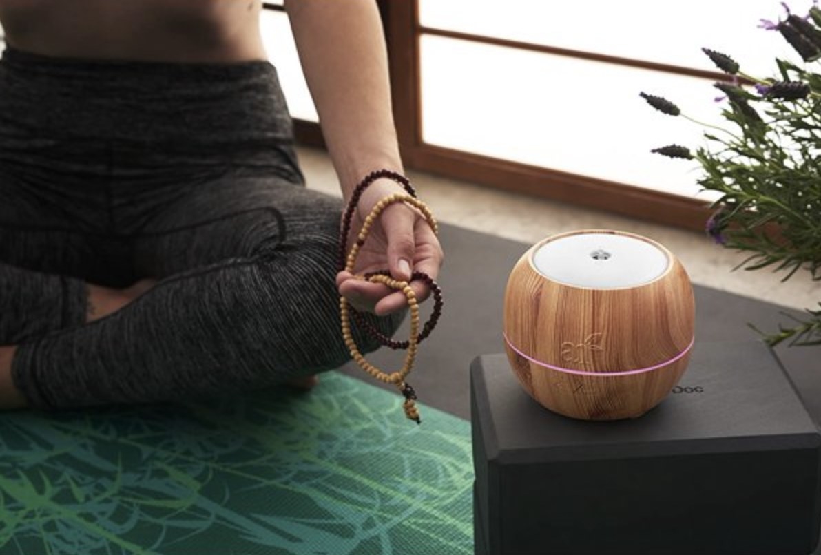 The brown wood diffuser on a yoga block next to someone meditating