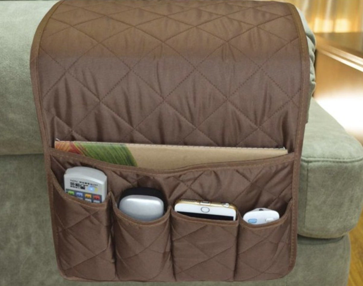 The brown caddy on a sofa armrest holding remote, glasses case, iphone, and journal