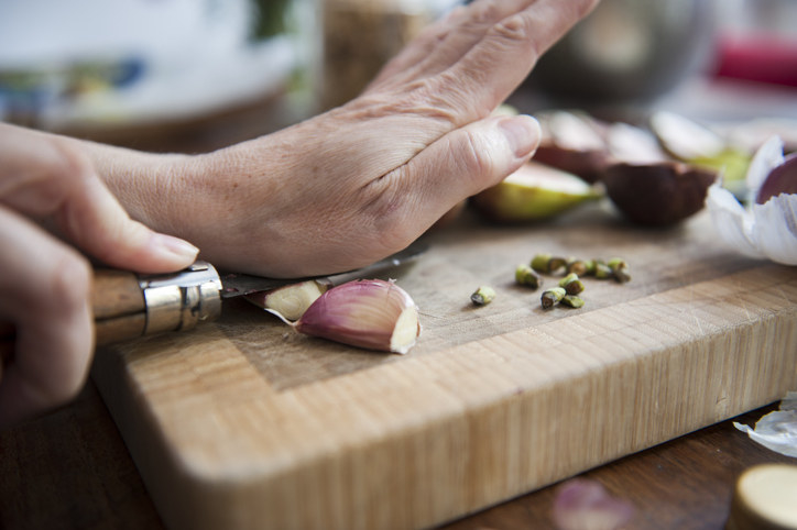 A person crushing garlic under a knife on a cutting board