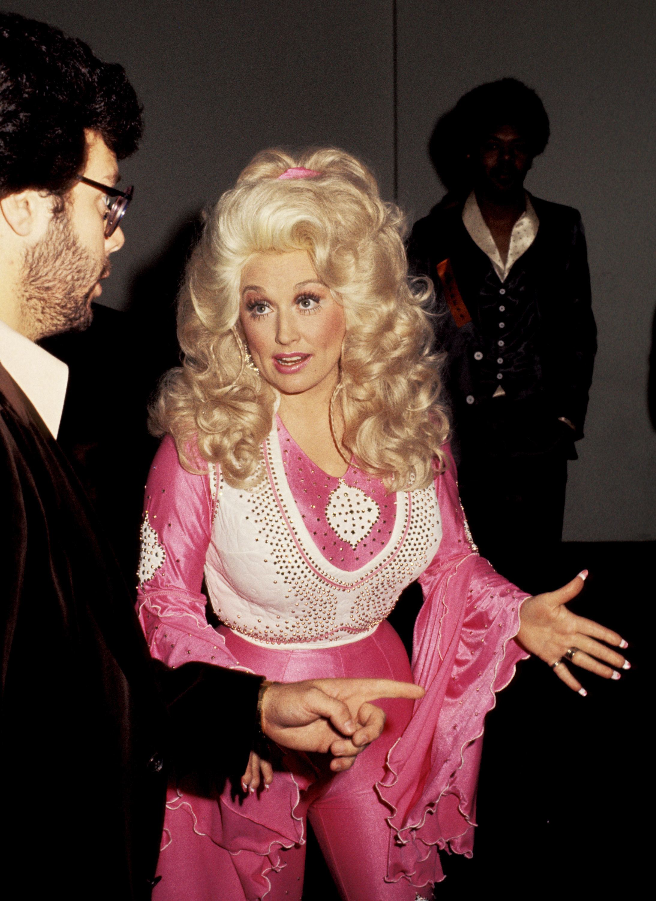 Dolly Parton at the 1977 Grammys in a tight pink jumpsuit with a white bedazzled vest