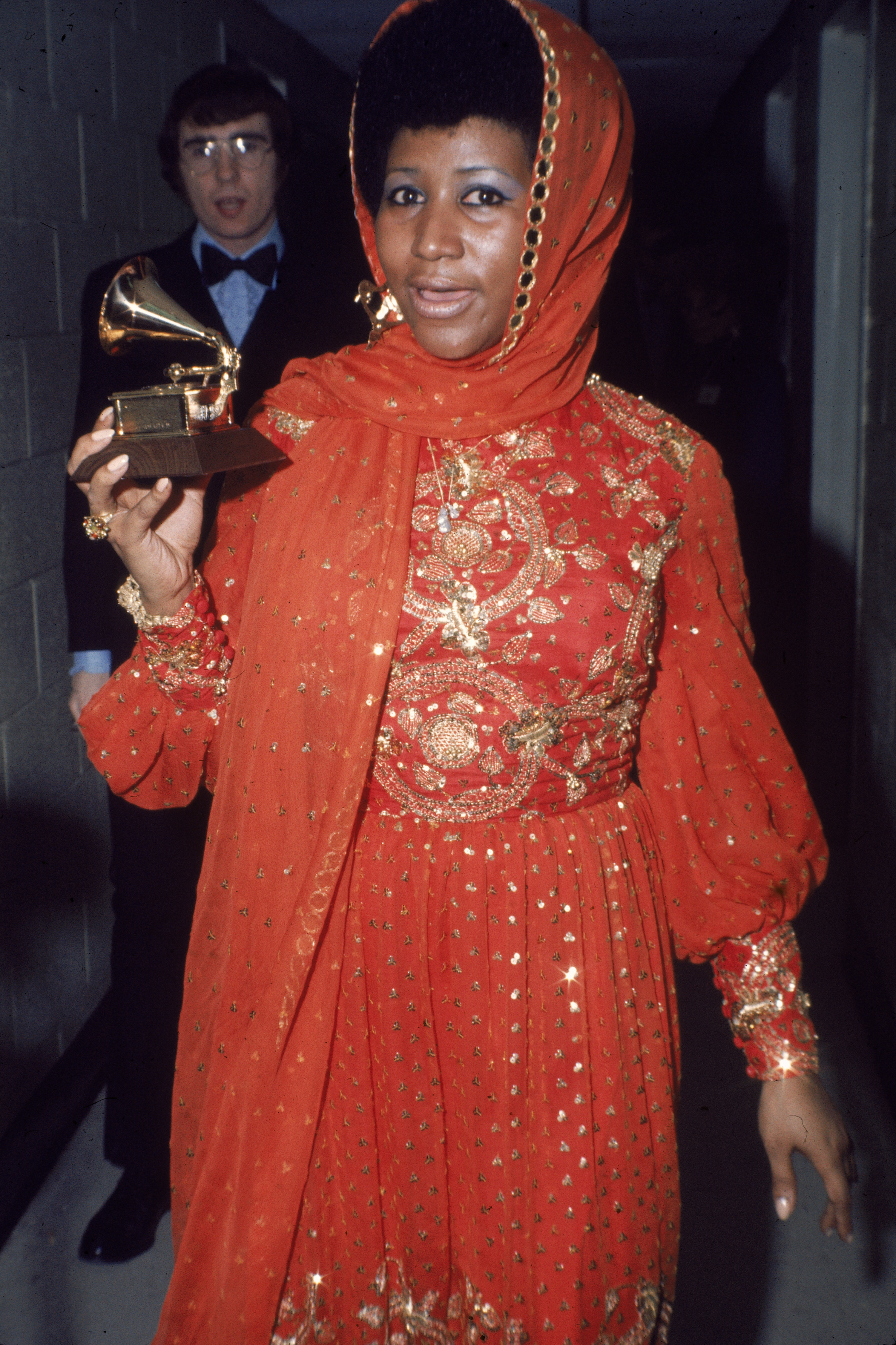 American soul singer Aretha Franklin stands backstage wearing an gold embroidered gown and holding a Grammy Award,