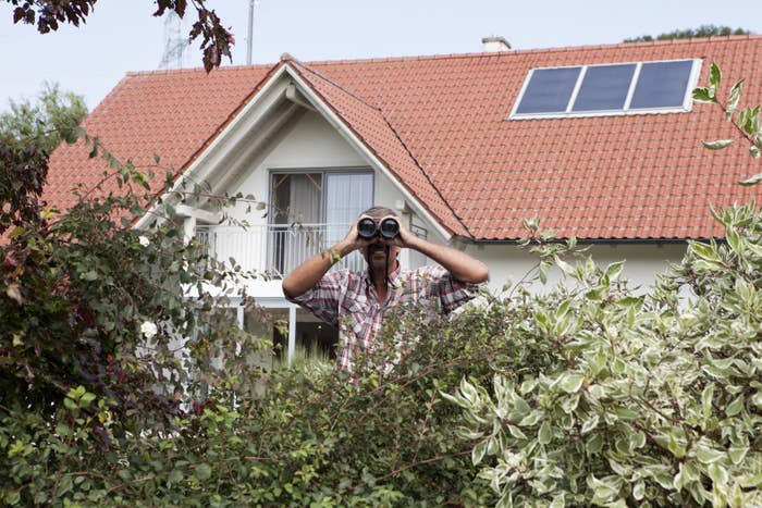 A man spies on his neighbors with binoculars