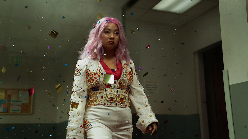Joy in a pink wig, wearing an Elvis-style jeweled jumpsuit and walking down a hallway with confetti flying