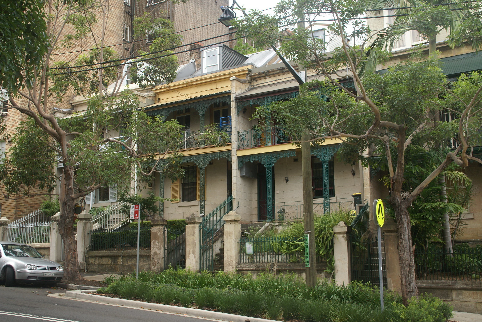 outside an older apartment building with two floors and trees surrounding