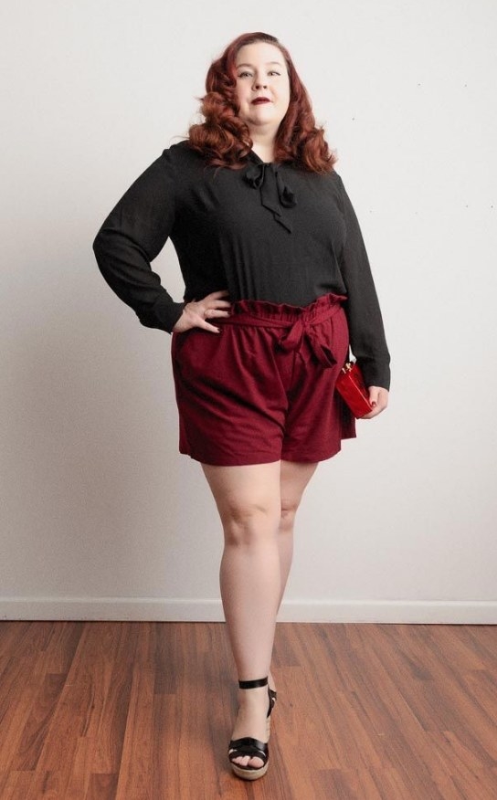 A reviewer wearing a pair of high waisted belted wine red shorts