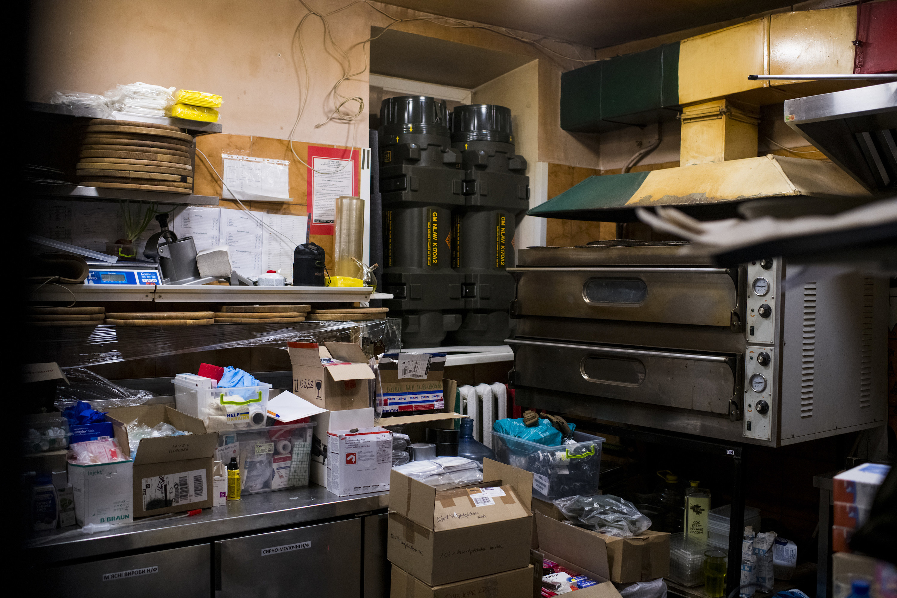 A crowded storage area showing an old pizza oven, shelves, boxes, and weapons against the wall
