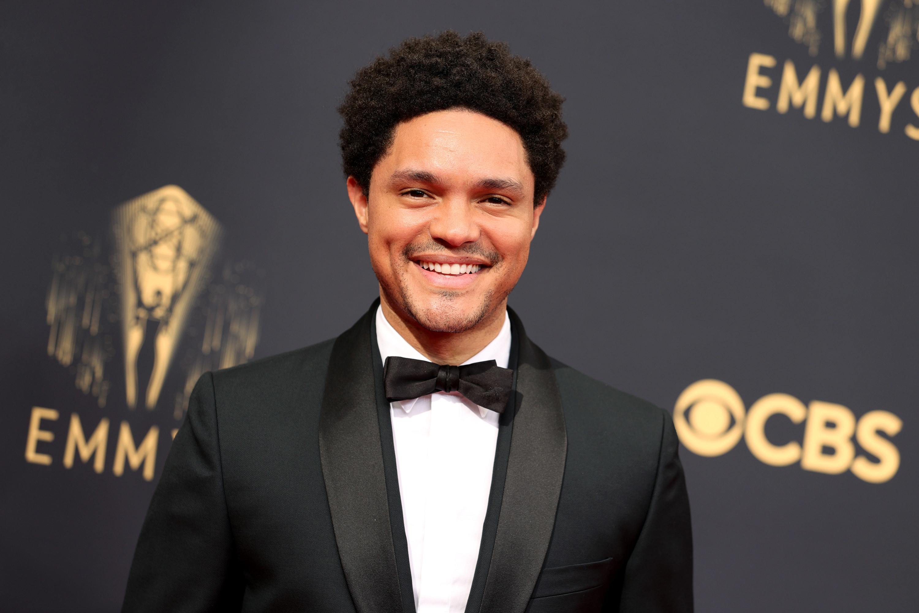 A close-up of Trevor Noah smiling in a bow tie and suit at the Emmy Awards red carpet