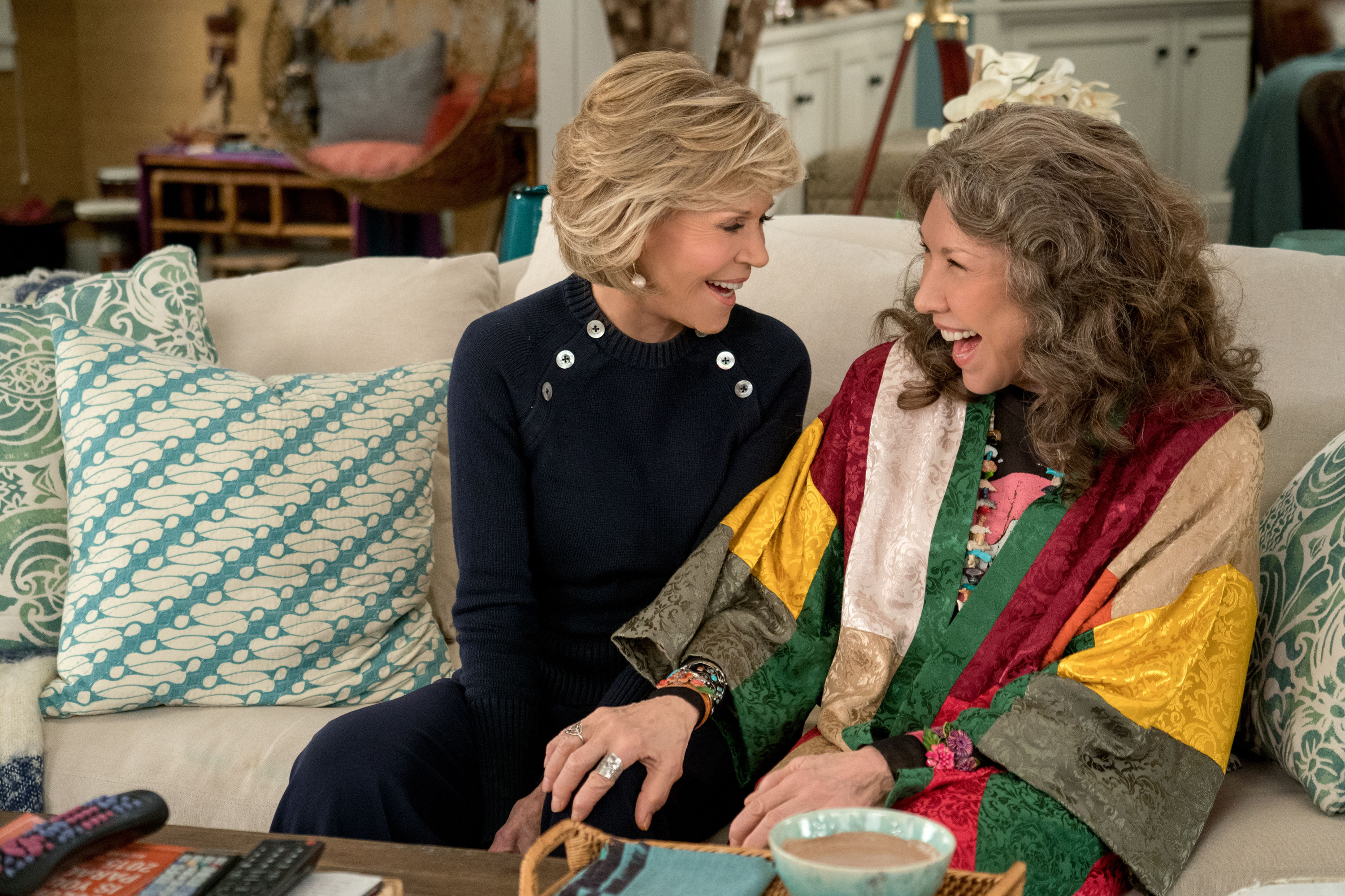 Two older women laugh while sitting on a couch.