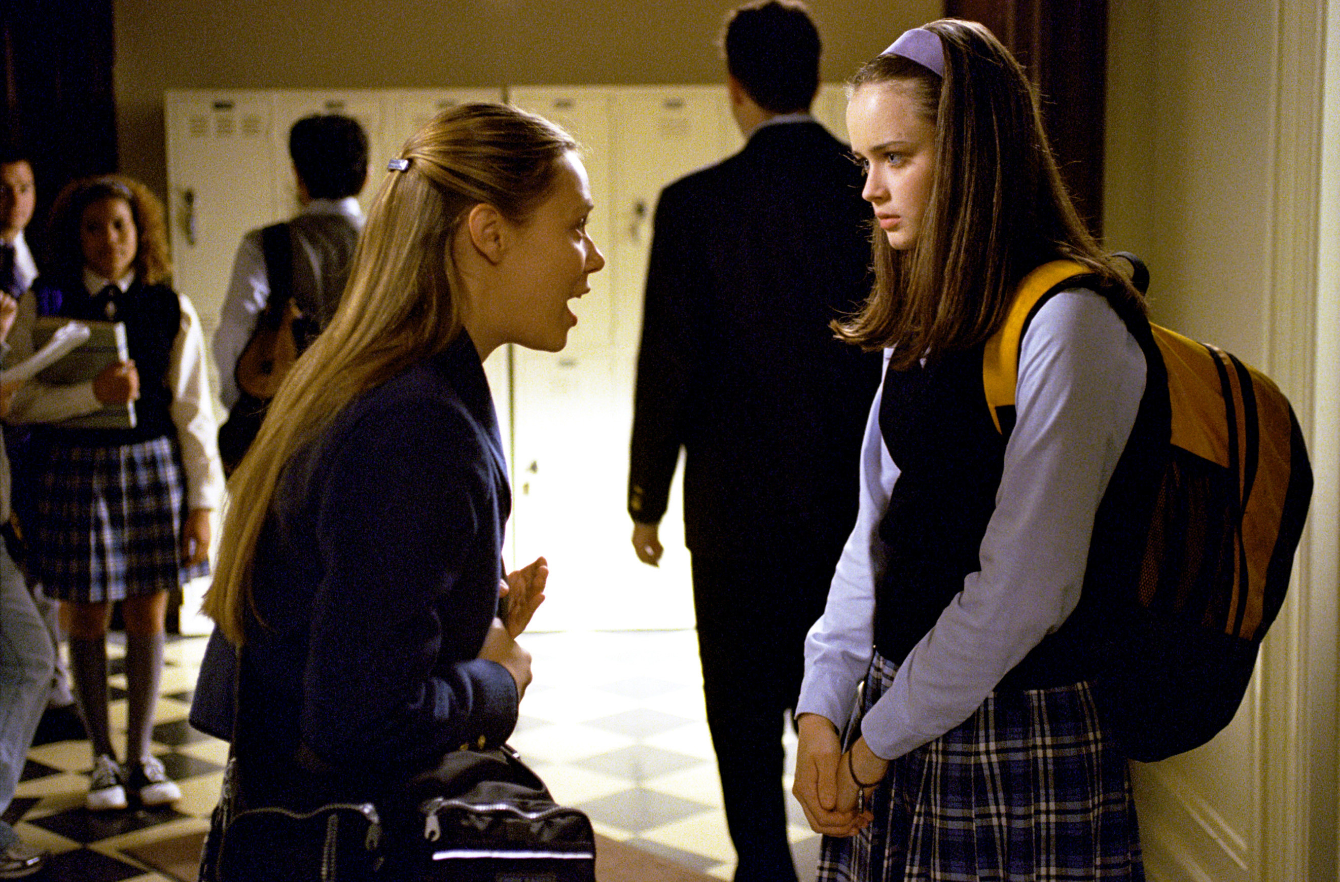 A blonde teenage girl yells at a brunette teenage girl. They both wear school uniforms.