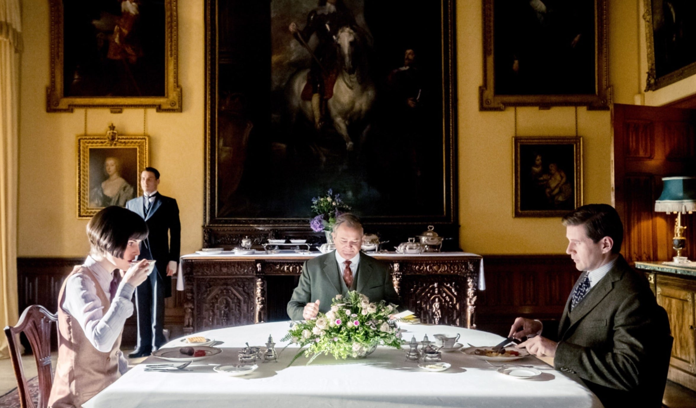 A woman and two men sit across the table from each other in a grand dinning room.