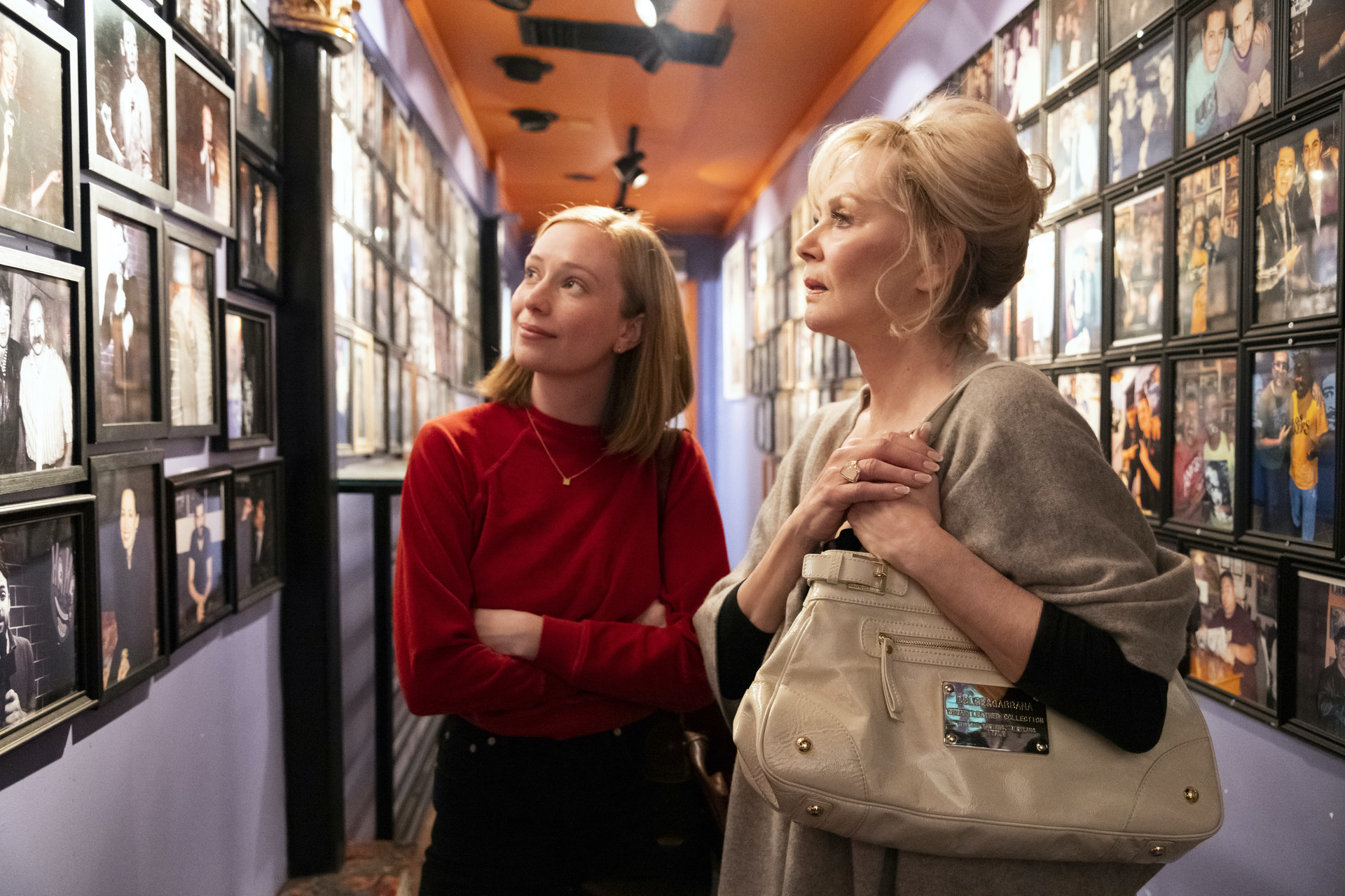 A young woman and an older woman look at pictures on a wall.