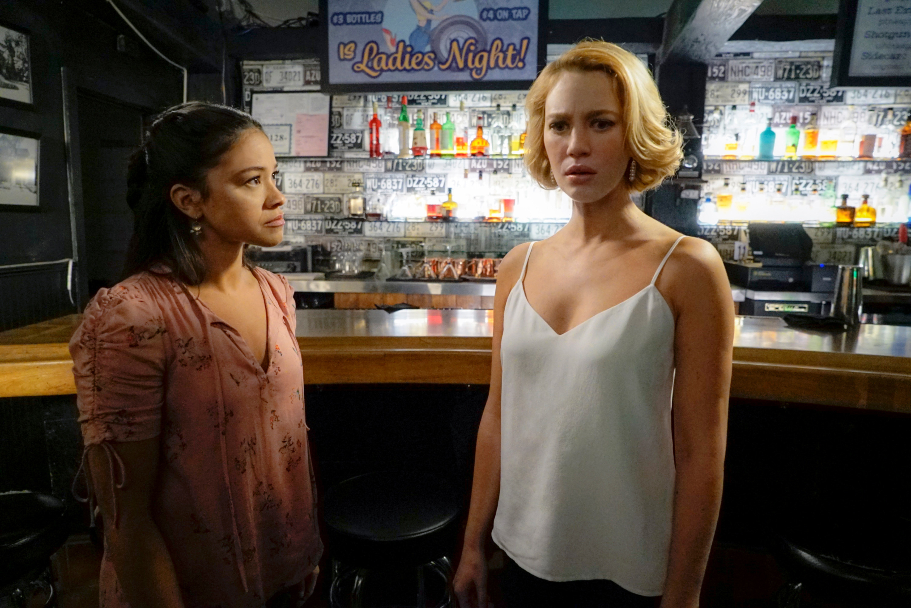 Two women stand in a bar, one looks worried.