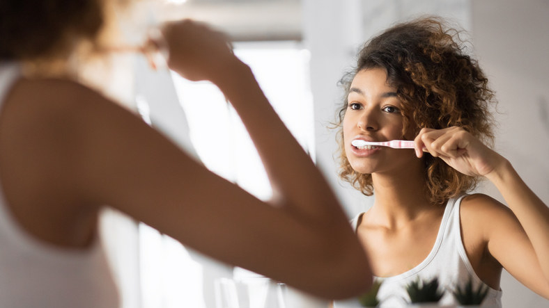 a woman brushes her teeth in the mirror