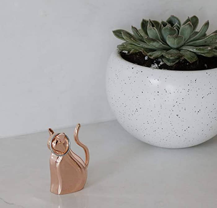 The copper cat on a marble counter holding a ring next to a potted plant