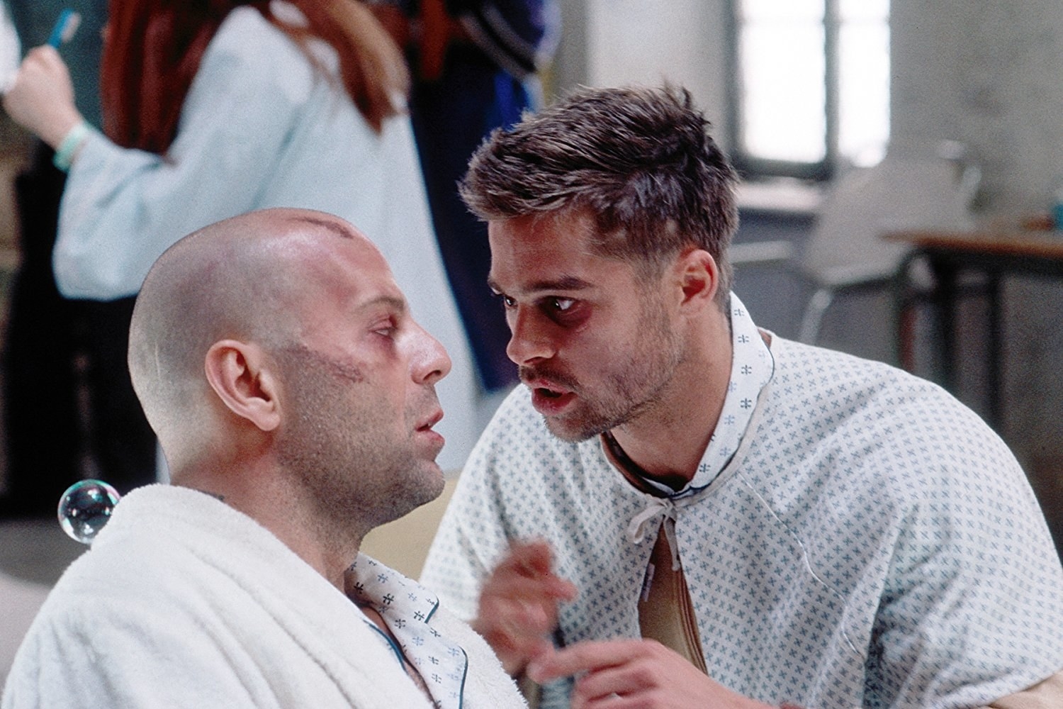 Bruce Willis as James Cole and Brad Pitt as Jeffrey Goines intensely looking at each other in an asylum
