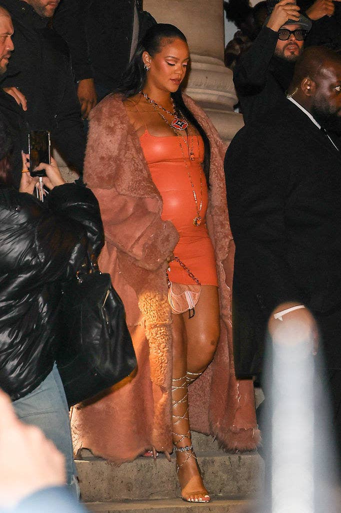 Rihanna walking down a set of steps at an event while rocking a short skintight spaghetti-strap dress, a long fur coat, and strappy heels