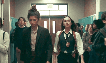 GIF of Rue and Lexi dressed as detectives walking down the hall in school