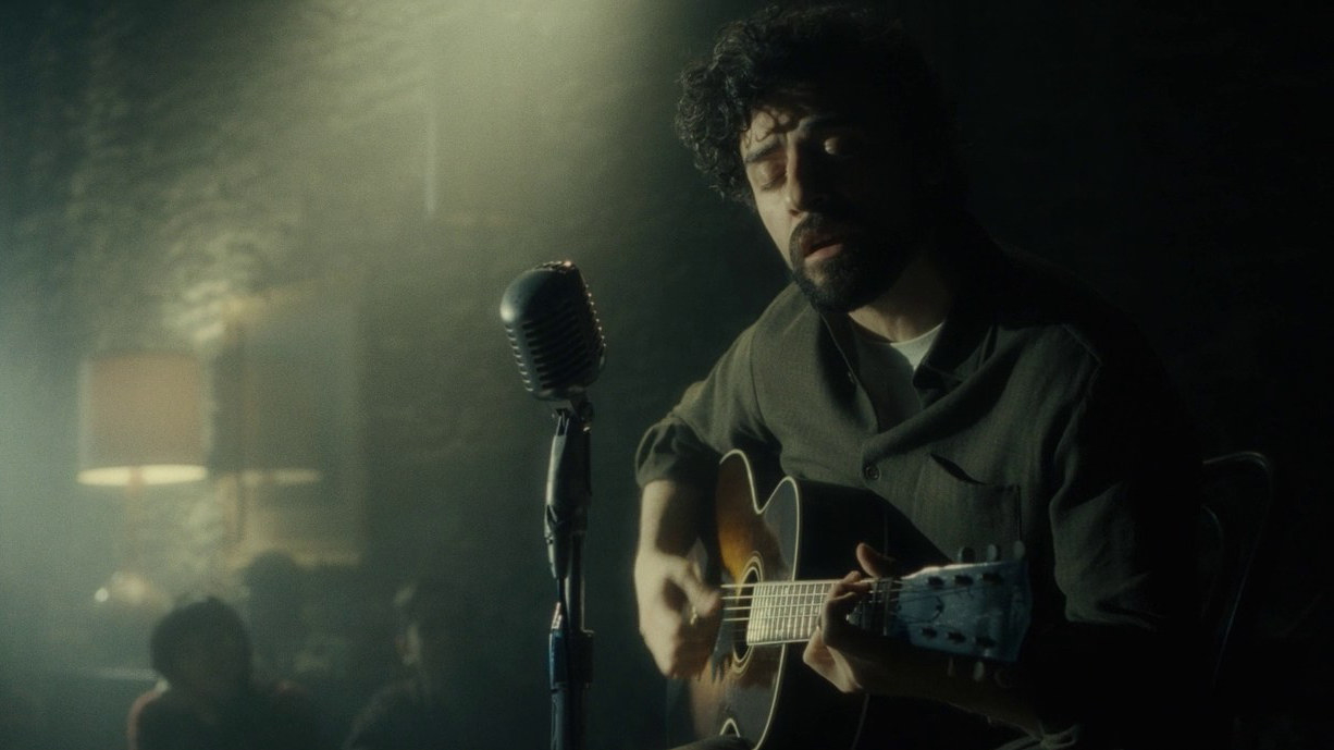 Oscar Isaac as Llewyn playing the guitar and singing into a mic