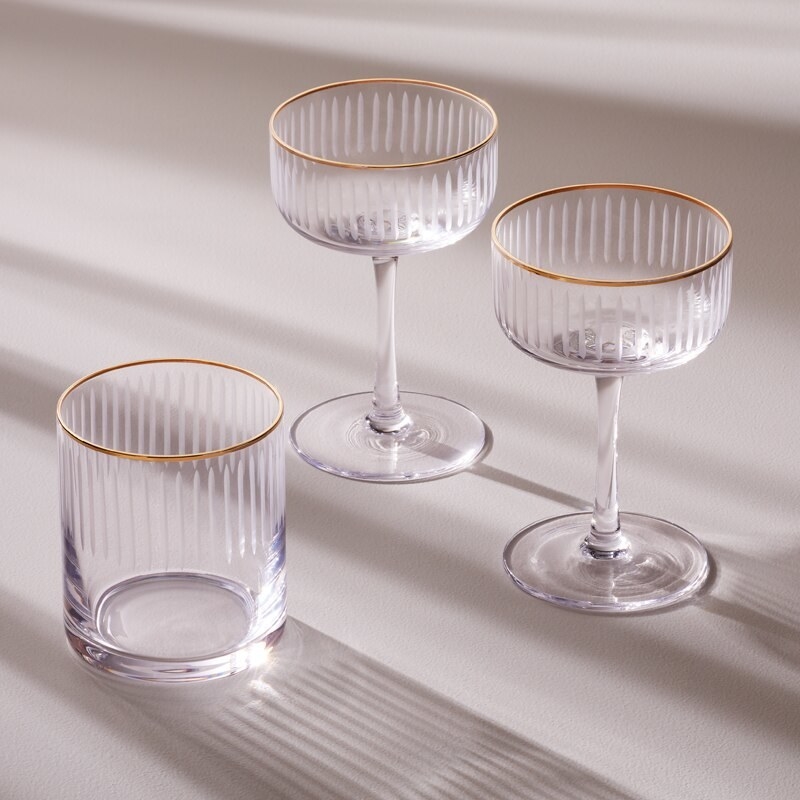 Two glass coupe glasses and a glass cup on a plain background