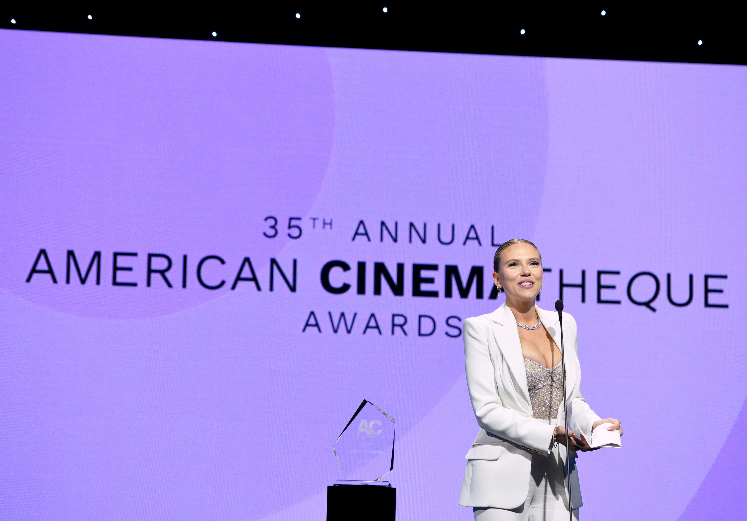 Scarlett behind a mic at the 35th American CinemaTheque Awards in a white suit