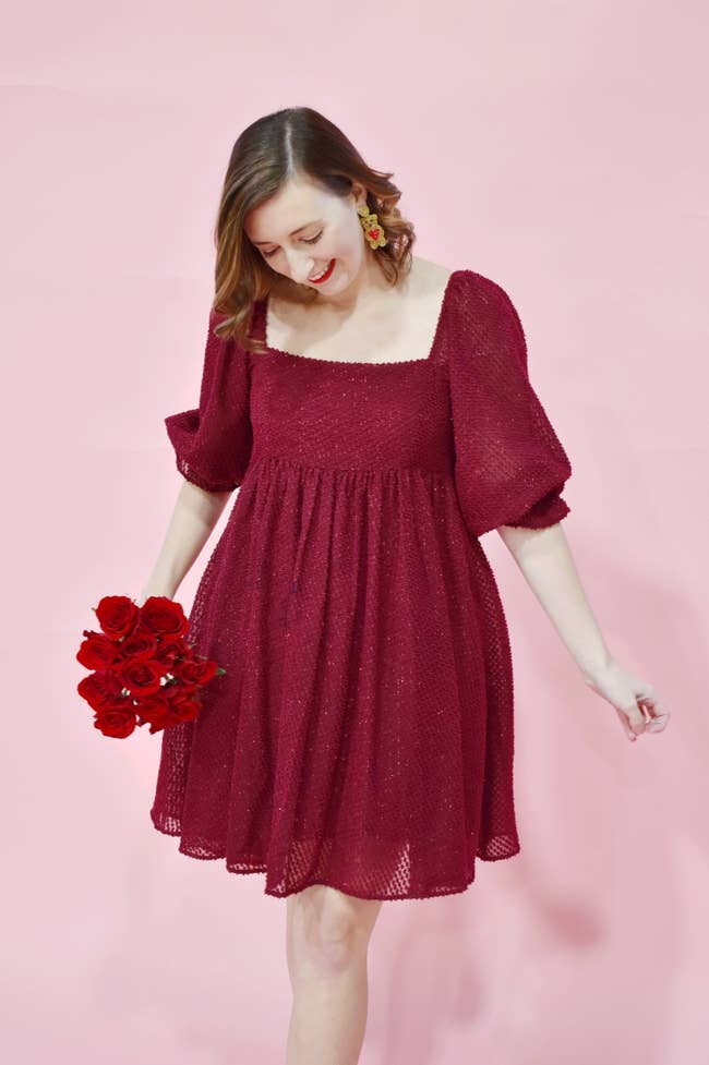 Model is wearing a burgundy colored short dress with a square neckline and 3/4 lantern sleeves