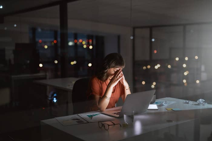 Woman working at her desk late at night, with hands on her head looking stressed
