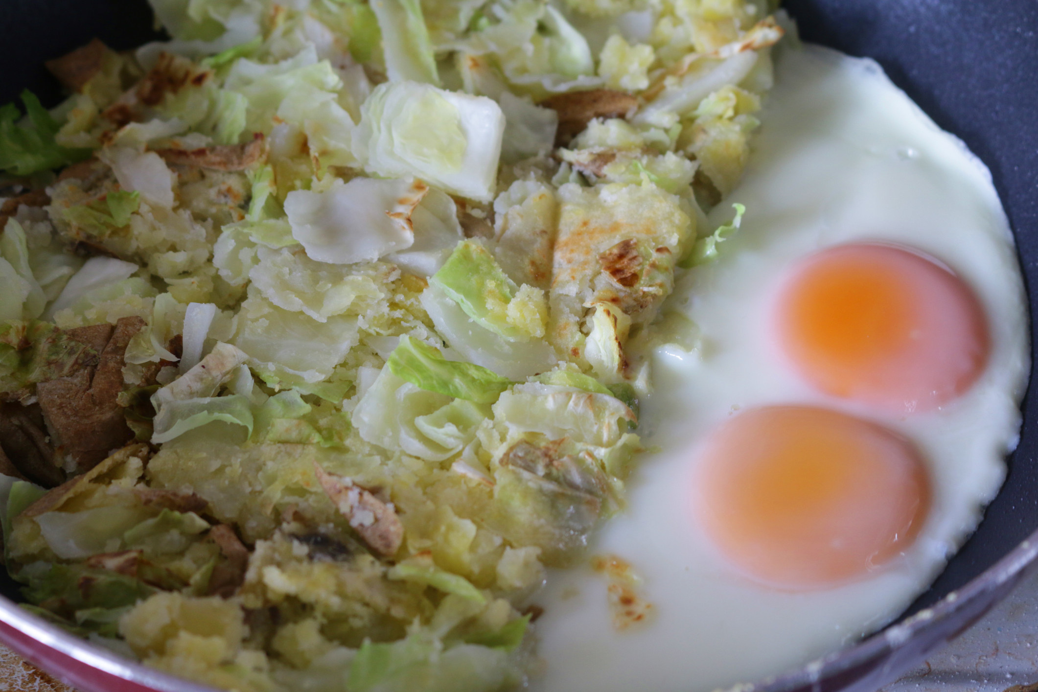 Leftover greens and meat in a skillet with fried eggs