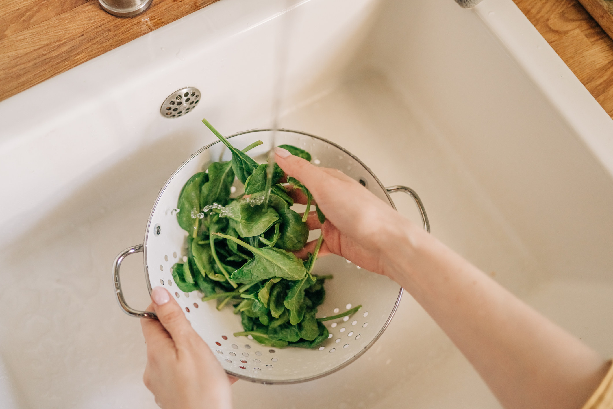 Female hands washing spinach vegetables at the kitchen sink