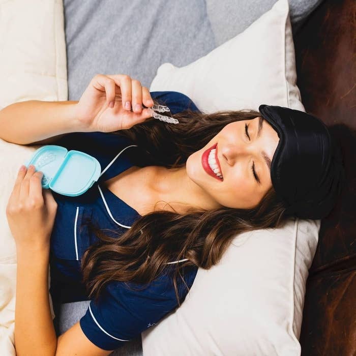 A person lying in bed holding their mouth guards