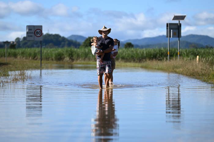A father holding his children as they inspect a flooded road near their home