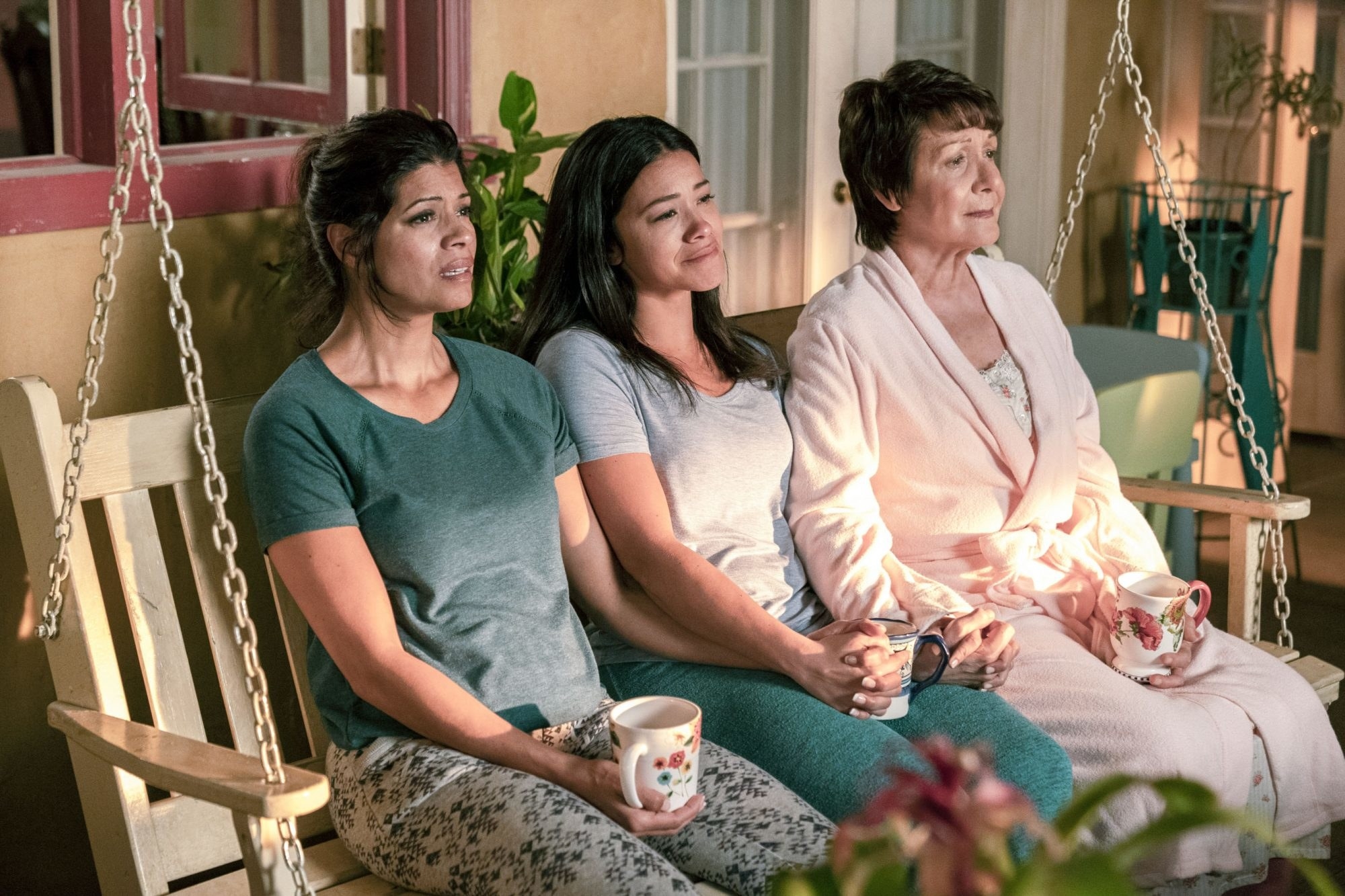 Jane, Xiomara, and Abuela sitting with matching coffee mugs in their hands and smiling with tears in their eyes