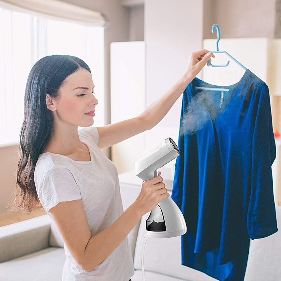 someone using the handheld steamer to remove wrinkles from a tunic shirt