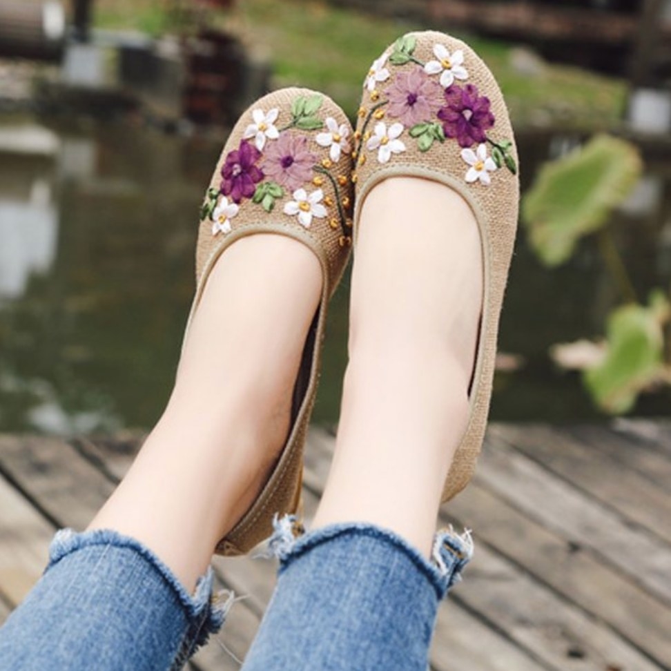 Model wearing khaki flats with pink, white, and purple flower embroidery