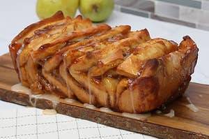 A side angle of pull apart bread with glaze drizzled over top, on a wood plank in a kitchen