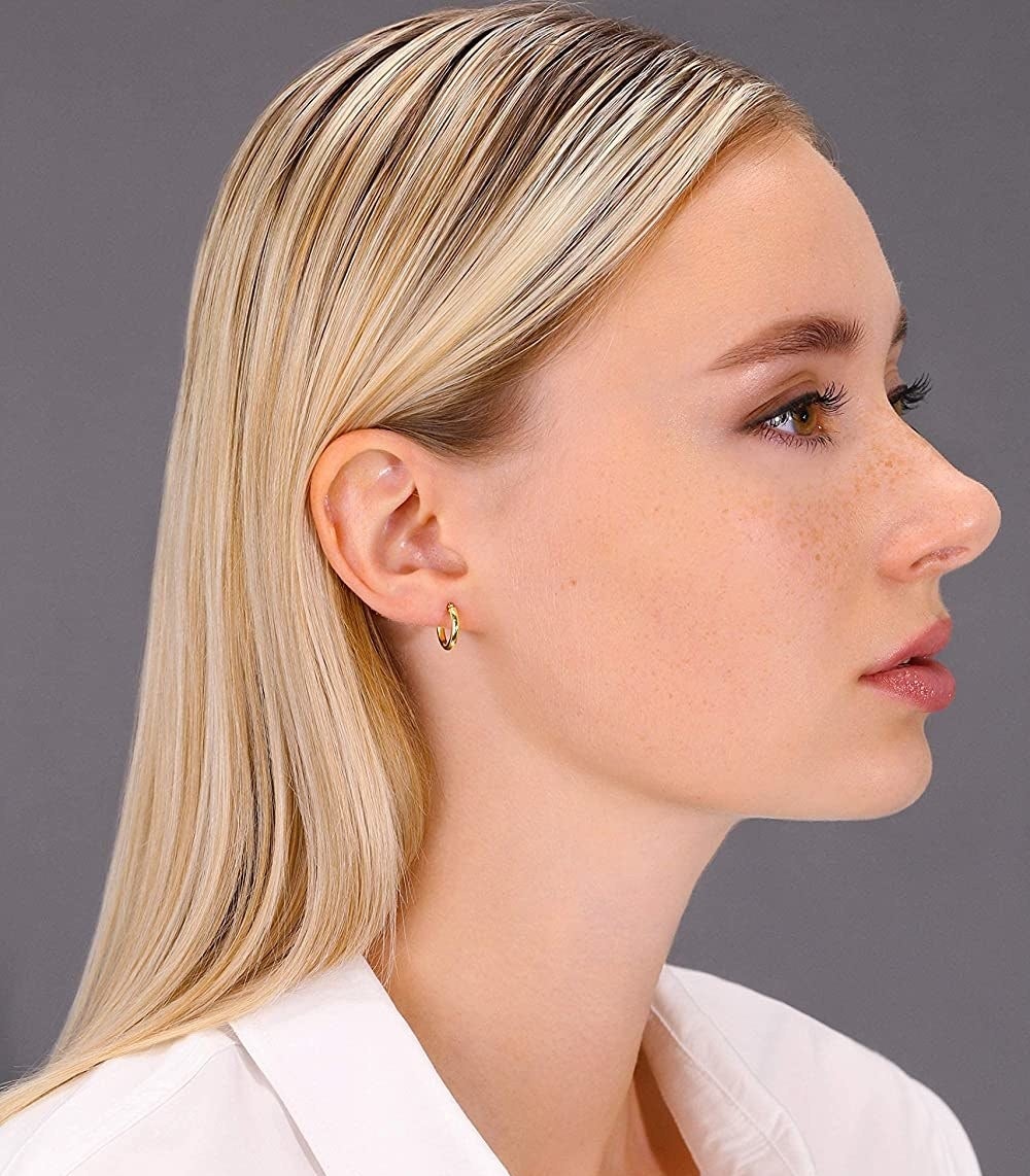 the profile of a person wearing the tiny gold hoops