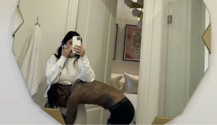 Kylie taking a mirror selfie as Travis cradles her midsection