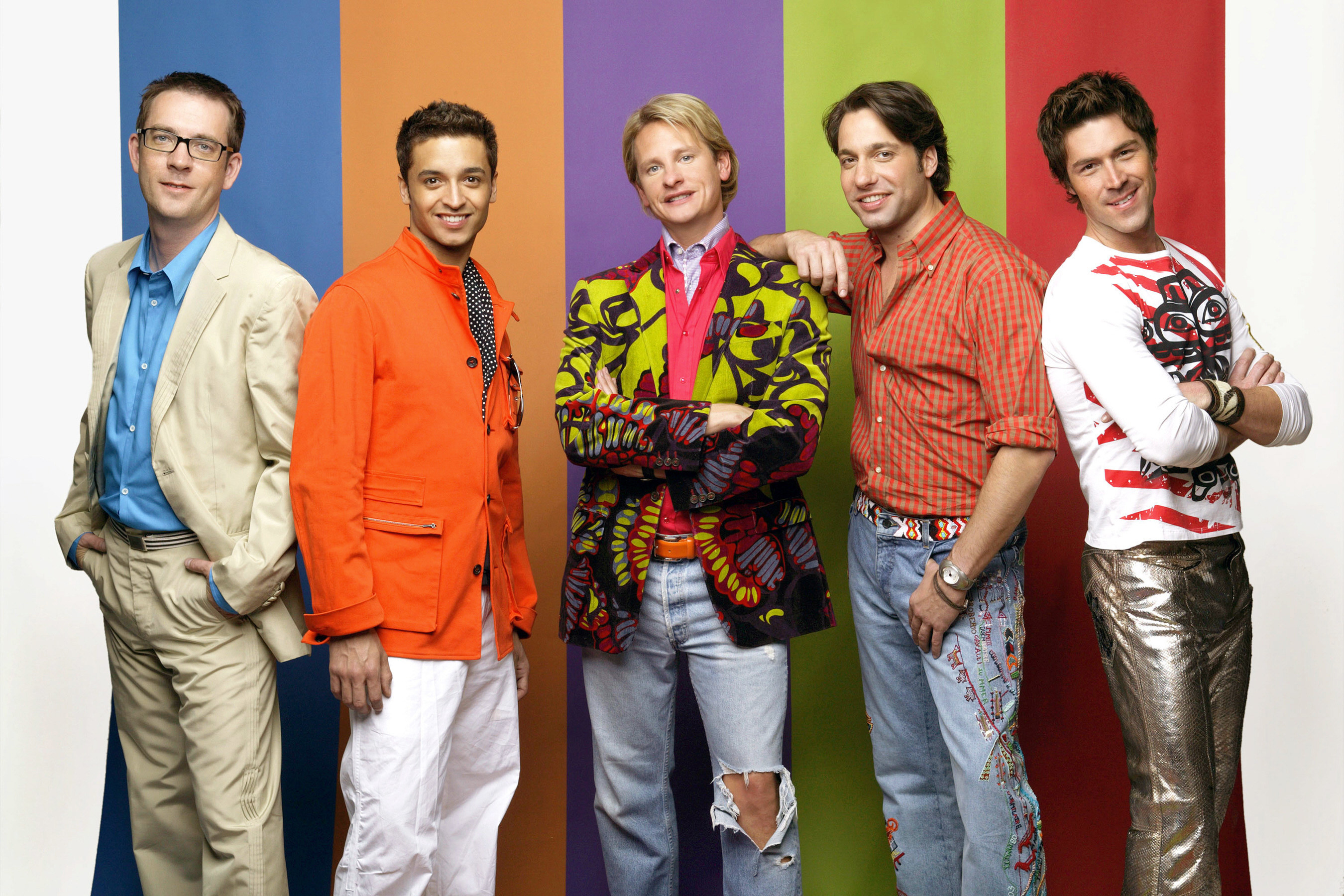 the cast posing in front of a rainbow background