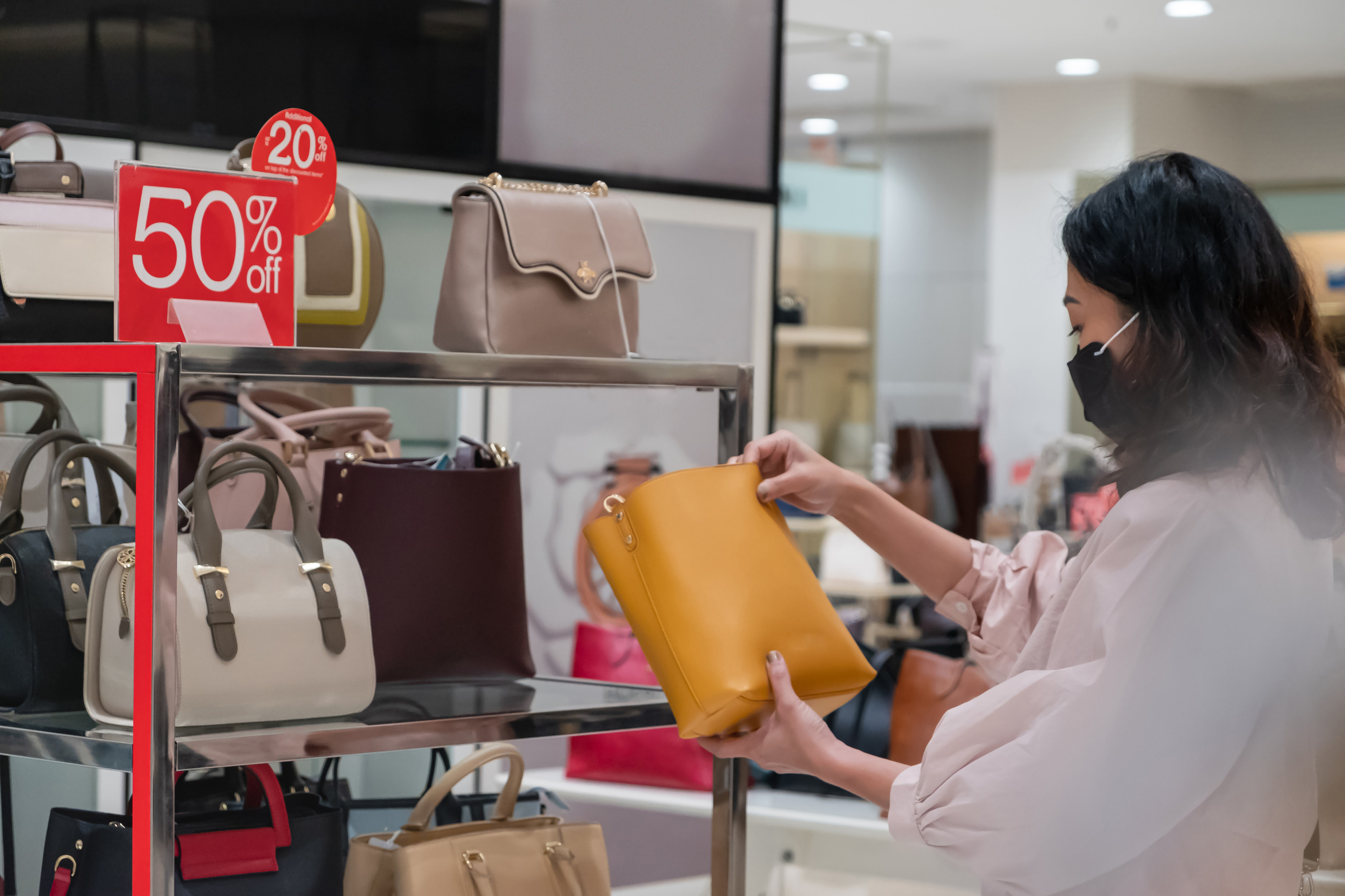A woman holding up a purse that is on the sale rack