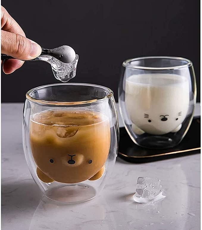 A person putting ice in the bear shaped cup filled with coffee